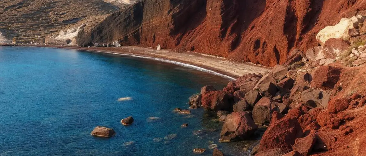 Red Beach in Akrotiri, Santorini, with rust-red volcanic cliffs, dark pebbles and clear blue Aegean water