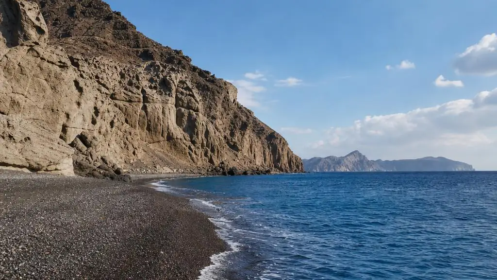 Remote Koloumbo Beach in northeast Santorini with dark volcanic pebbles, rugged cliffs and open Aegean Sea